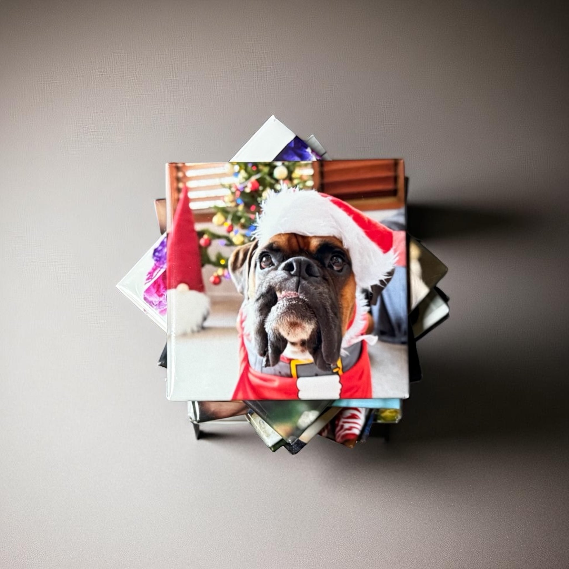 Square photo magnet of a dog wearing a Santa hat lying on top of a stack of photo magnets on a gray background